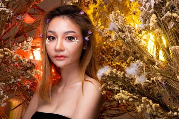 Beautiful romantic young Asian woman in Fox tail in bush variety of flowers posing on background fresh and dried flora. Inspiration of autumn winter snow Perfume, cosmetics concept.