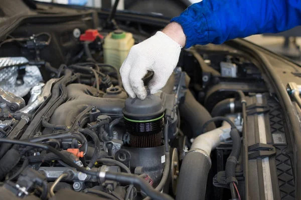 車サービスでの車の修理 オイルフィルターを車のエンジンに交換します オイルフィルターを保持するプロの整備士の手 技術写真 — ストック写真