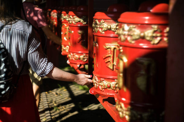 girl twists a prayer drum in a Buddhist temple. Red khurde in the sun. Mani drum