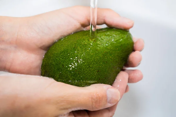 Lavar las frutas con agua corriente. Manos y aguacate bajo un chorro de agua —  Fotos de Stock