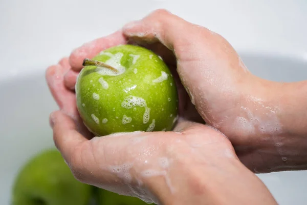 씻는 과일. 소녀는 사과를 씻는다. 손 과 비눗물 이 많은 녹색 사과 로열티 프리 스톡 이미지