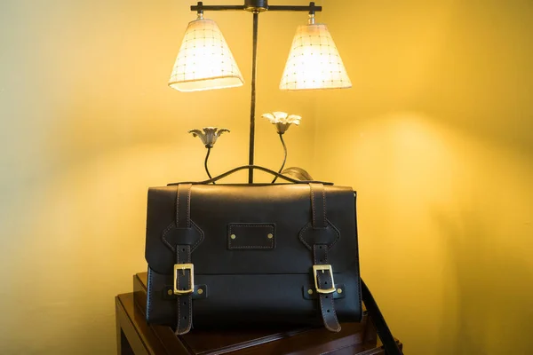 Handmade black leather bag on the background of an expensive lamp.