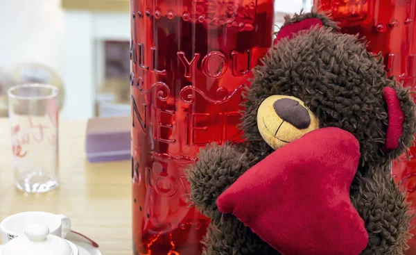 Medvídek se srdcem na pozadí červené skleněných lahví. — Stock fotografie