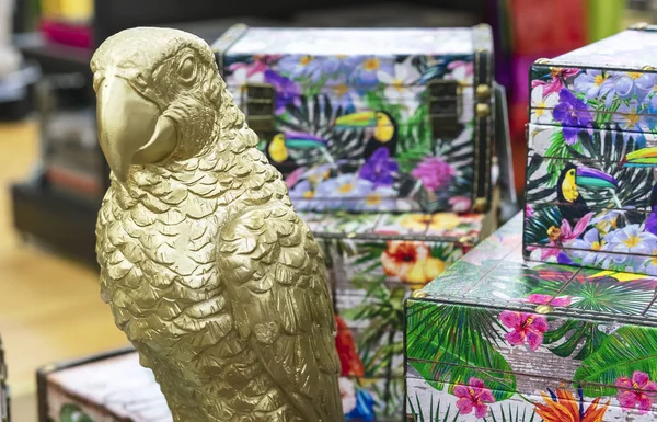 Золотая статуэтка попугая на фоне красочных сундуков в сувенирном магазине . — стоковое фото