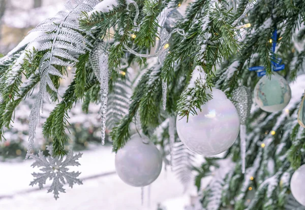 Der schneebedeckte Weihnachtsbaum ist mit weißen Kugeln, Eiszapfen und einem Kranz geschmückt. — Stockfoto