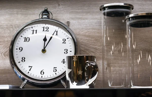 Relógio despertador com caneca e frascos de vidro em um fundo de madeira . — Fotografia de Stock