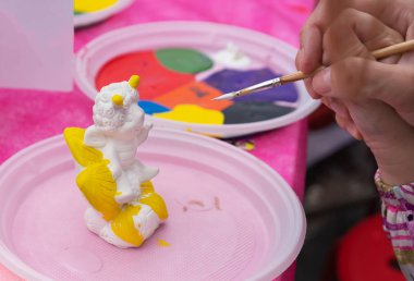 Çocuk parlak renklerle seramik bir heykelcik boyar. Boyama için seramik staruette.