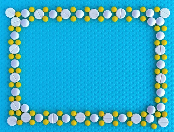 흰색 알약과 파란색 배경에 프레임 형태의 둥근 노란색 비타민. 의료 개념. — 스톡 사진