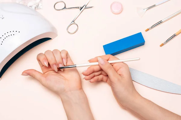 Las manos de una chica haciendo una manicura, aplicando gel con un cepillo. la vista desde la parte superior —  Fotos de Stock