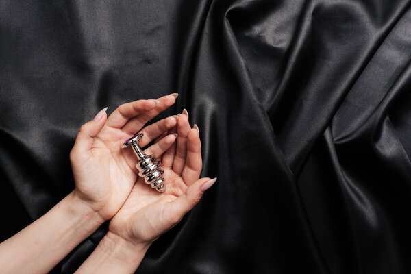 female hands in handcuffs on a dark silk sheet with an anal plug