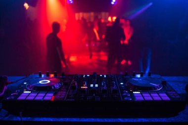 DJ konsolu, bir gece kulübünde dans eden bulanık insanlarla müziği karıştırır.