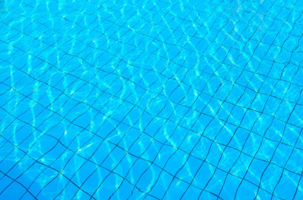 Tiled bottom of pool under transparent blue water with patches of sunlight, background