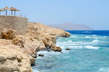 Plaj şemsiyeleri üzerinde kayalık sahil, Kızıldeniz, Sharm El Sheikh, Mısır. Dalga sonları taş