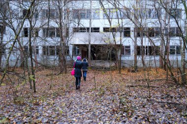 PRIPYAT, UKRAINE - NOVEMBER 11, 2018: Unknown tourists go to abandoned school building in dead ghost town of Pripyat in Chernobyl NPP alienation zone, Ukraine clipart