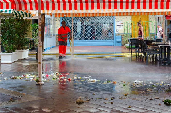 Man is watering paving slabs with water from hose, removing garbage on territory of market in Nice, France — Stock Photo, Image