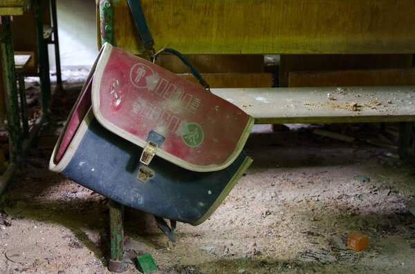 Старая грязная школьная сумка висит на школьном столе в заброшенной начальной школе в деревне Дронки в зоне отчуждения Чернобыльской АЭС, Хойникский район, Беларусь