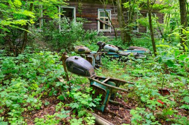 DRONKI, BELARUS - 4 Temmuz 2020: Çernobil nükleer enerji santralinin kapsama alanı dışında kalan Dronki köyündeki terk edilmiş ilkokulun ahşap binasının yakınındaki paslı motosiklet iskeletleri