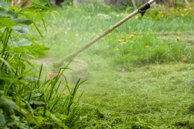 Bir adam çimleri bir gaz biçme makinesiyle biçiyor.