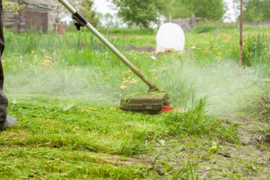Bir adam çimleri bir gaz biçme makinesiyle biçiyor.