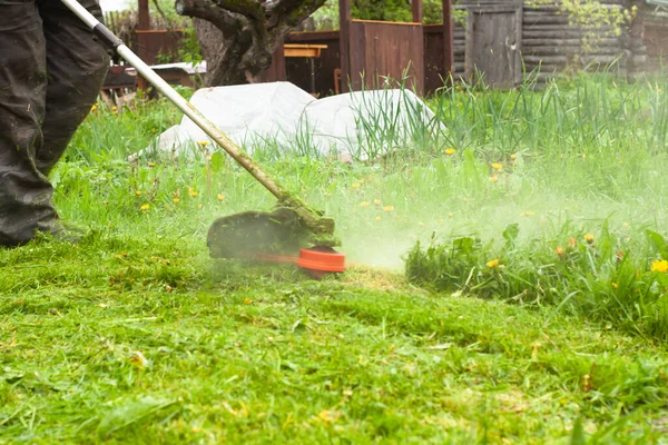 a man mows the lawn with a gas mower with a fishing line