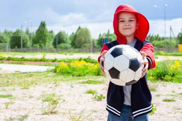 Kırmızı ceketli bir çocuk topu tutuyor. Çocuklar oynamak ister. Çocuklarla oyna