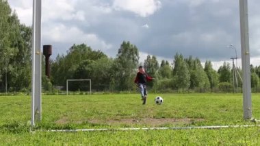 Bir çocuk futbol oynuyor. Topu kaleye doğru itiyor.