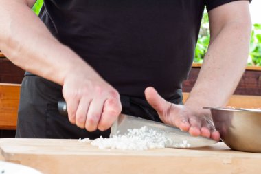 Şef soğanı kızartılmak için keser. Eller çerçevede bir bıçakla.