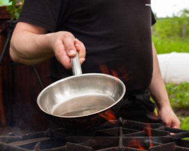 Aşçı tavayı ateşin üstünde ısıtır. Mutfak ızgarada.