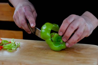Aşçı ahşap bir tahtada yeşil biberleri şeritler halinde keser.