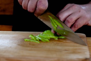 Aşçı ahşap bir tahtada yeşil biberleri şeritler halinde keser.