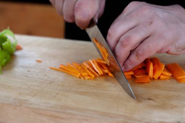 Aşçı ahşap bir tahtanın üzerinde havuçları parçalara ayırır.