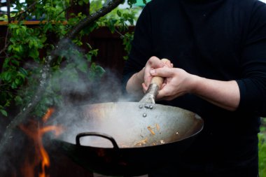 Aşçı soğan, havuç ve tavukla ahşap bir spatulayı karıştırır.