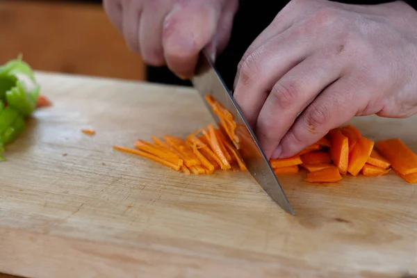 Aşçı ahşap bir tahtanın üzerinde havuçları parçalara ayırır.