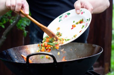 Aşçı, ateşte tavukla sebzeleri karıştırır. Asya mutfağı