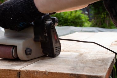 Siyah eldivenli bir adam zımpara makinesiyle tahtayı öğütüyor. ahşap işleri