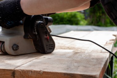 Siyah eldivenli bir adam zımpara makinesiyle tahtayı öğütüyor. ahşap işleri