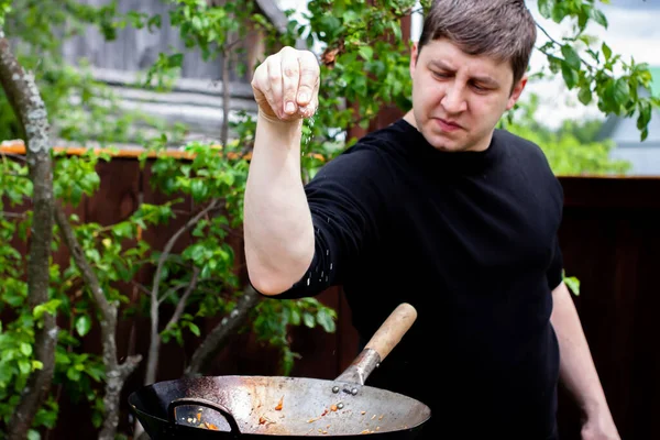 Aşçı tavadaki yemeği tuzlar. Doğada yemek pişirmek. ateş