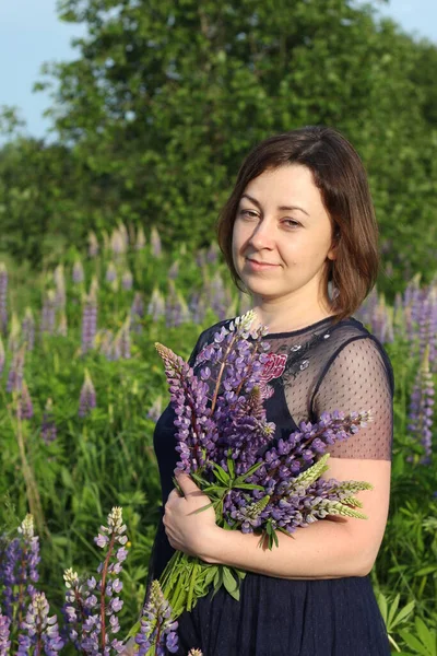 Genç ve güzel bir kız Lupin çiçekleriyle tarlada
