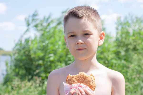 少年は自然の中でおいしいハンバーガーを食べる — ストック写真