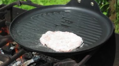 Aşçı, tavada pirzola pişirir. Doğada yemek yapmak.