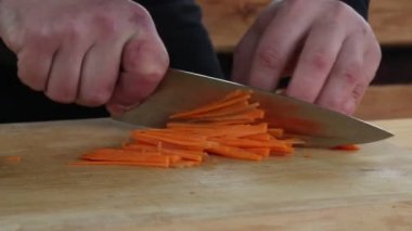 Aşçı ahşap bir tahtanın üzerinde havucu parçalara ayırıyor.