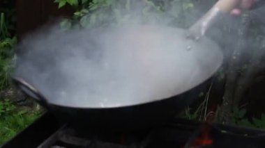 Aşçı ateşte tavada yemek hazırlar. Kızarmış et, erişteli sebze.