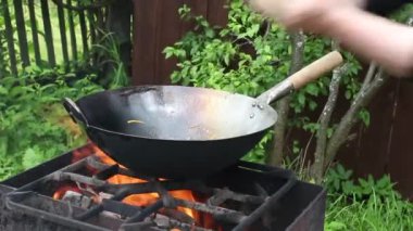 Aşçı ateşte tavada yemek hazırlar. Kızarmış et, erişteli sebze.