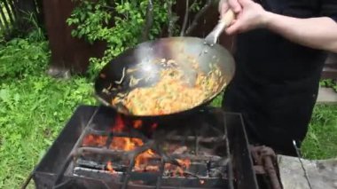 Aşçı ateşte tavada yemek hazırlar. Kızarmış et, erişteli sebze.