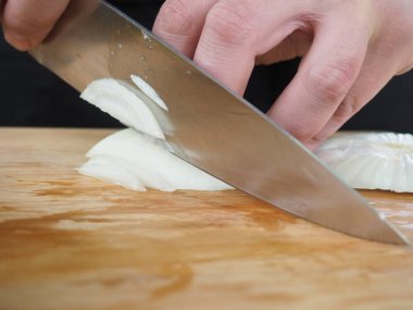 Aşçı ahşap bir tahtada soğan kesiyor. poster.