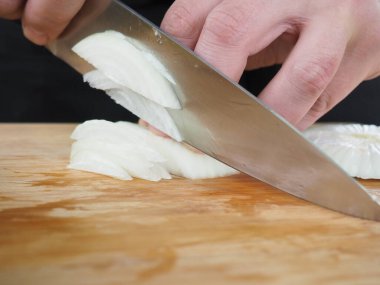 Aşçı ahşap bir tahtada soğan kesiyor. poster.