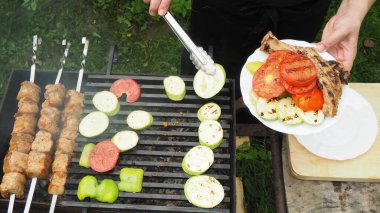 Aşçı sebze ve eti tabakta maşayla ızgaradan kaldırır. Lezzetli yemek.