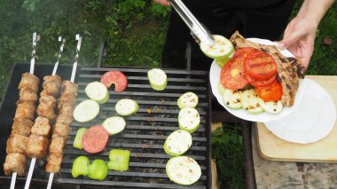Aşçı sebze ve eti tabakta maşayla ızgaradan kaldırır. Lezzetli yemek.