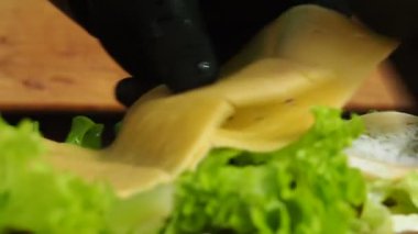 Eldivenli bir şef büyük bir sandviçe marul yaprağı koyar. 4K video.