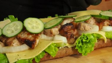 Eldivenli bir şef taze marul yaprakları üzerinde et, domates ve peynirli bir sandviç hazırlar. 4K video.